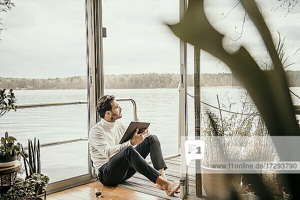Male professional looking away while holding digital tablet in houseboat