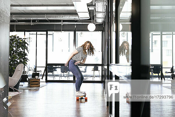 Lächelnde weibliche Fachkraft beim Skateboardfahren im Büro