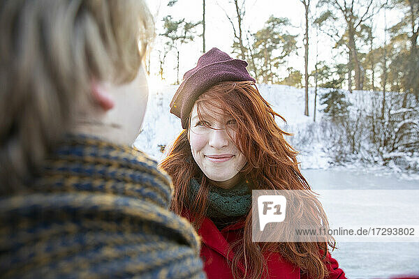 Lächelnde rothaarige Frau mit Strickmütze sieht ihren Freund an
