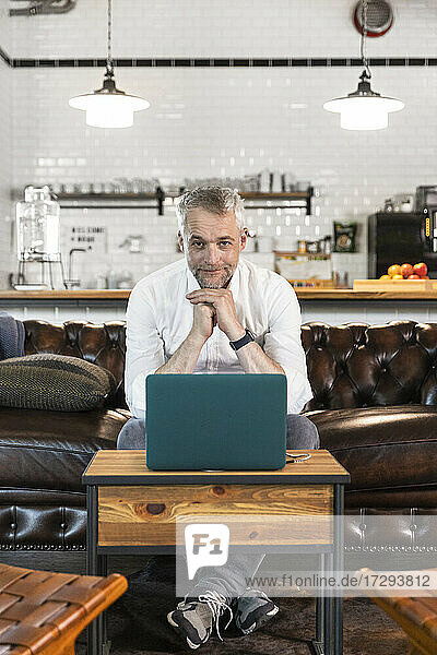 Male professional with hand on chin sitting in front of laptop at office cafeteria