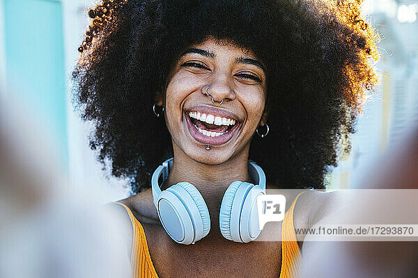 Cheerful young Afro woman wearing headphones taking selfie