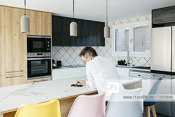 Businessman using mobile phone while sitting at kitchen island at home