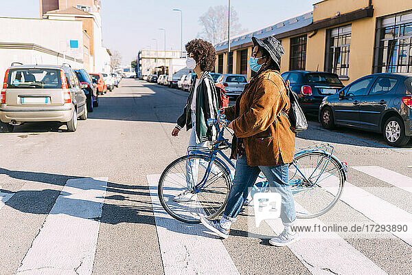 Female friends with bicycle crossing road in city