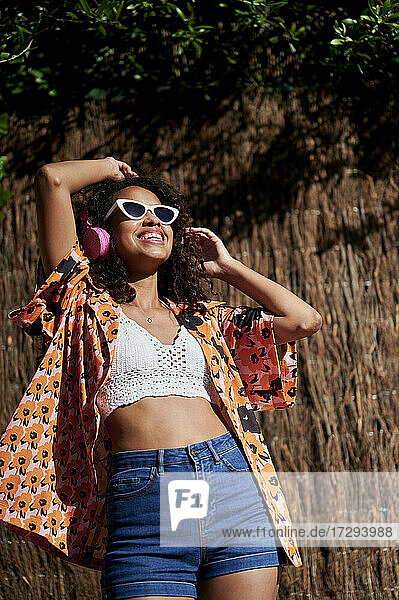 Lächelnde Frau hört Musik über Kopfhörer beim Tanzen an einem sonnigen Tag