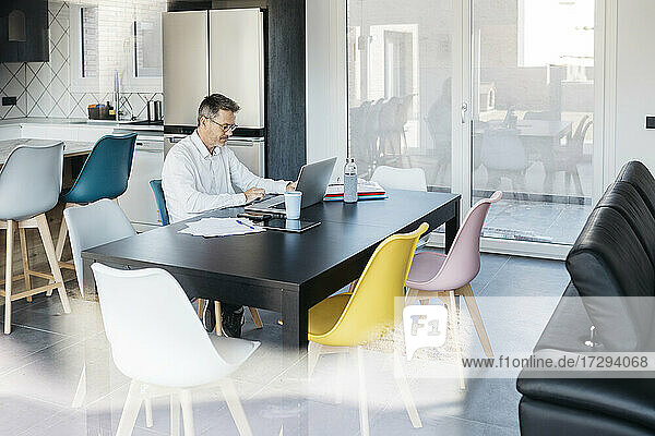 Geschäftsmann  der einen Laptop benutzt  während er am Tisch im Heimbüro sitzt