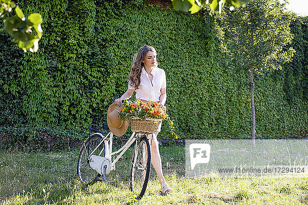 Junge Frau  die bei einem sonnigen Spaziergang im Garten ein Fahrrad schiebt