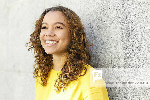Lächelnde junge Frau träumt vor einer Wand
