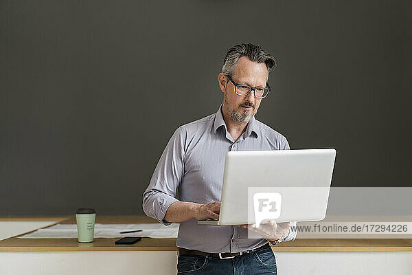 Männlicher Unternehmer  der im Stehen im Büro einen Laptop benutzt