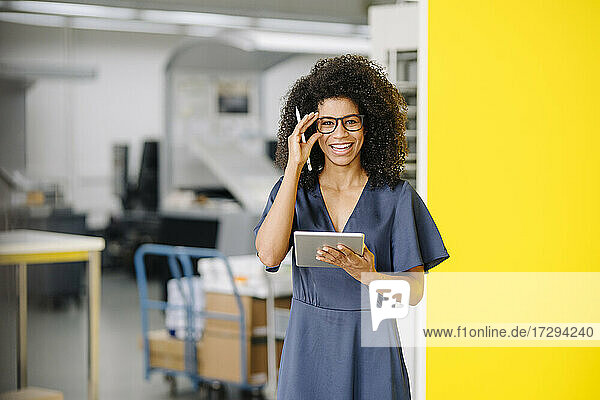 Lächelnde Geschäftsfrau mit digitalem Tablet  die eine Brille im Büro einstellt