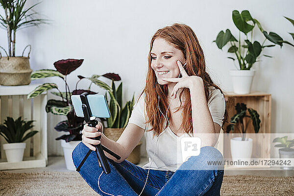 Schöne Frau lächelnd während Videoanruf durch Smartphone auf dem Boden zu Hause