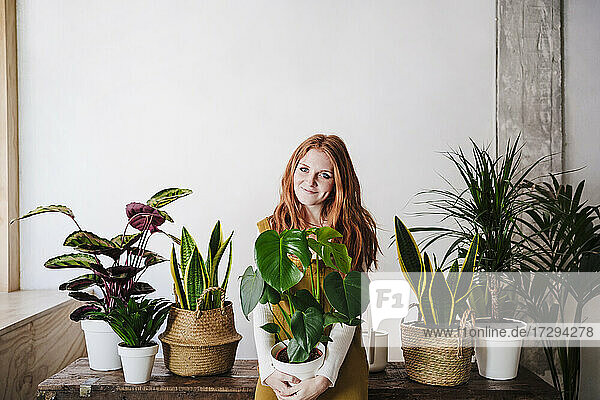 Smiling redhead woman holding potted plant at home