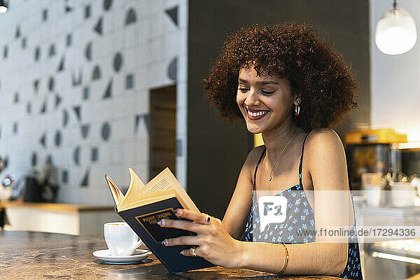 Smiling student reading book while sitting at cafe