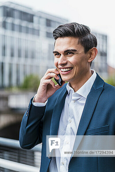 Lächelnder männlicher Berufstätiger  der wegschaut  während er mit einem Smartphone telefoniert
