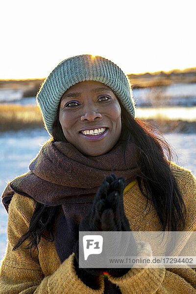Lächelnde reife Frau mit Schal steht mit verschränkten Händen im Winter