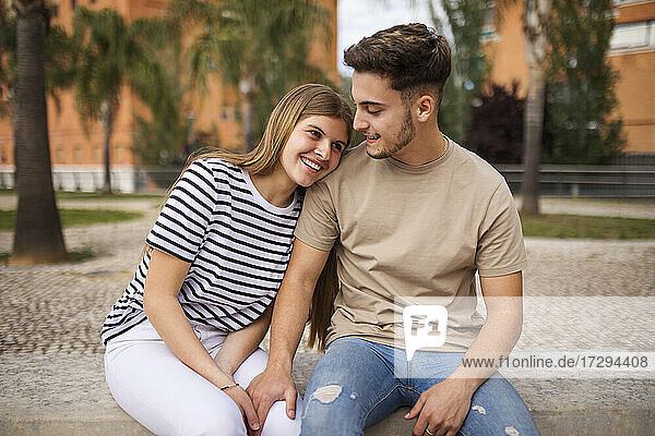 Smiling girlfriend with head on shoulder of boyfriend sitting in park