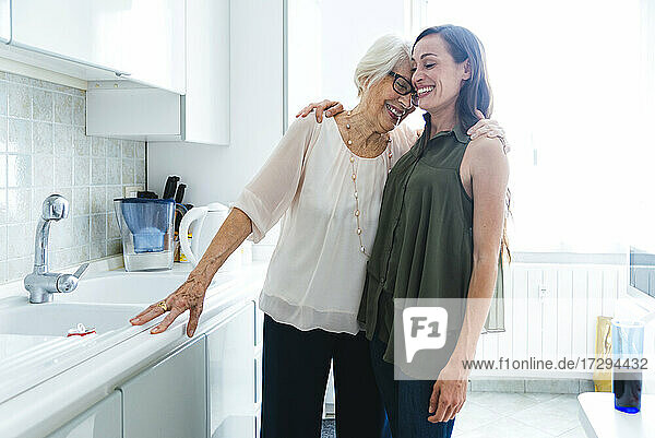 Lächelnde Enkelin und Großmutter  die sich in der Küche zu Hause umarmen