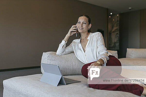 Smiling mature businesswoman talking on mobile phone while sitting on sofa