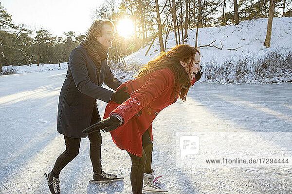 Junger Mann hilft seiner Freundin beim Schlittschuhlaufen auf einem zugefrorenen See