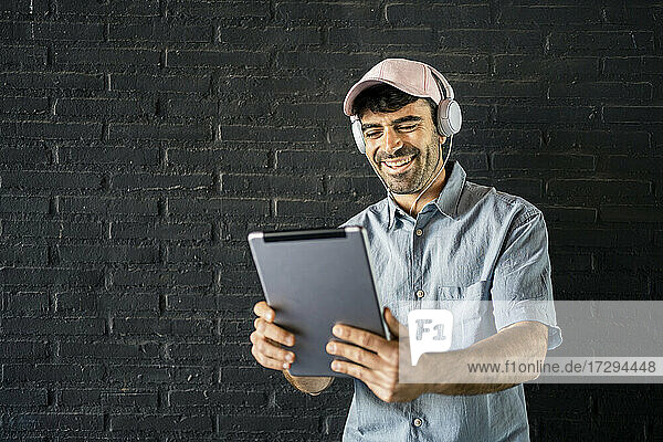 Glücklicher junger Mann mit digitalem Tablet vor einer Wand