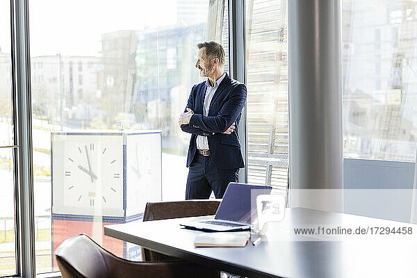 Businessman with arms crossed looking through window in office