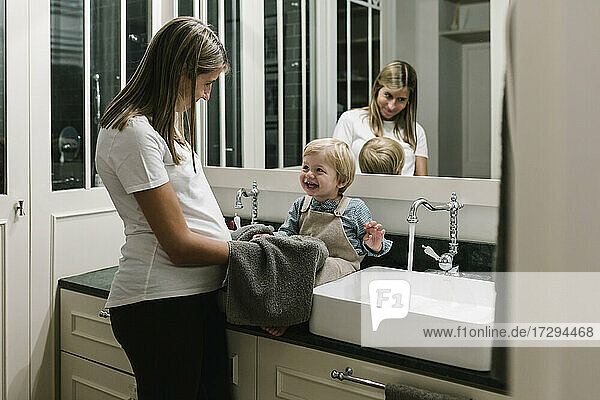 Schwangere Frau trocknet die Hände ihres Sohnes mit einem Handtuch im Badezimmer zu Hause