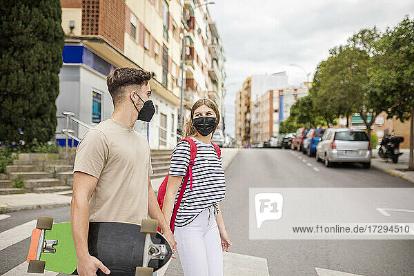 Ehepaar mit Gesichtsschutz beim Überqueren der Straße in der Stadt während des COVID-19-Ausbruchs