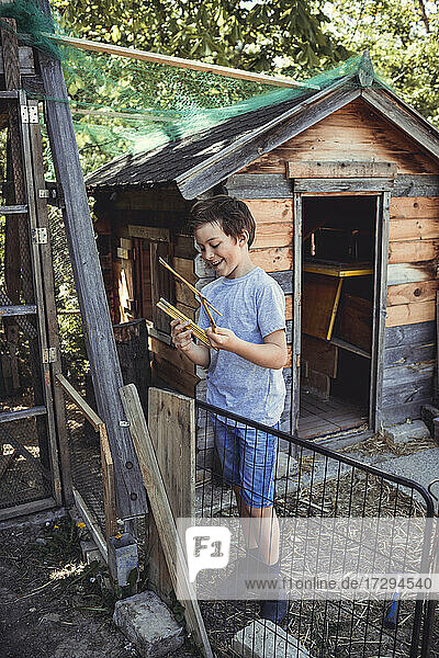 Lächelnder Junge hält Werkzeug beim Bau eines Kaninchenstalls im Hinterhof