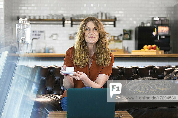 Female professional holding coffee cup while sitting on sofa at cafeteria in office