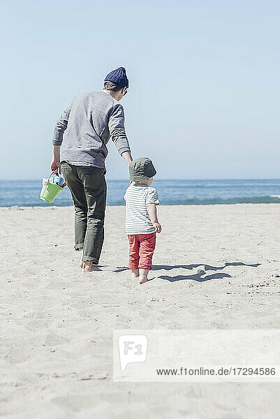 Sohn geht mit Vater am Strand spazieren und hält sich an den Händen