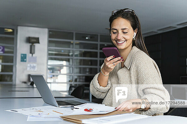 Smiling businesswoman sending voicemail through mobile phone at office