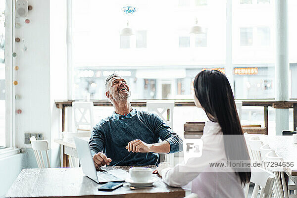 Lächelnder Geschäftsmann schaut auf eine Drohne  während er mit einem Kollegen im Café sitzt