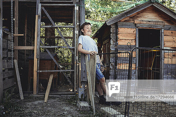 Smiling boy standing by rabbit hutch in back yard