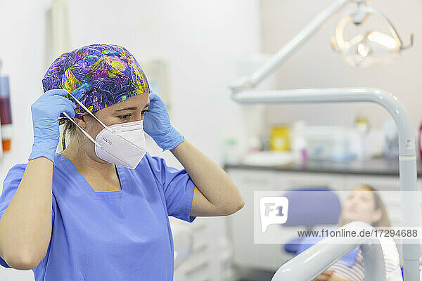 Zahnärztin beim Entfernen der Gesichtsschutzmaske mit Patient im Hintergrund in einer medizinischen Klinik