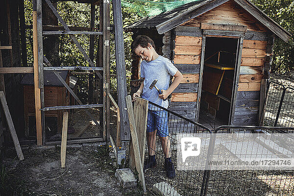 Junge hämmert Holz für den Bau eines Kaninchenstalls