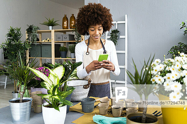 Lächelnde Blumenhändlerin  die ein Mobiltelefon benutzt  während sie an einem Tisch in einem Pflanzengeschäft steht