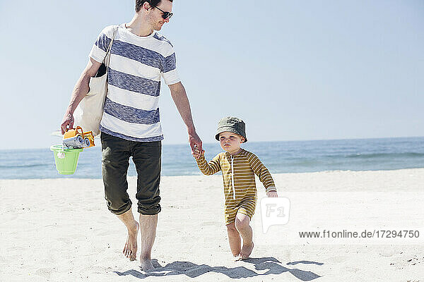 Junge mit Hut geht mit seinem Vater am Strand spazieren