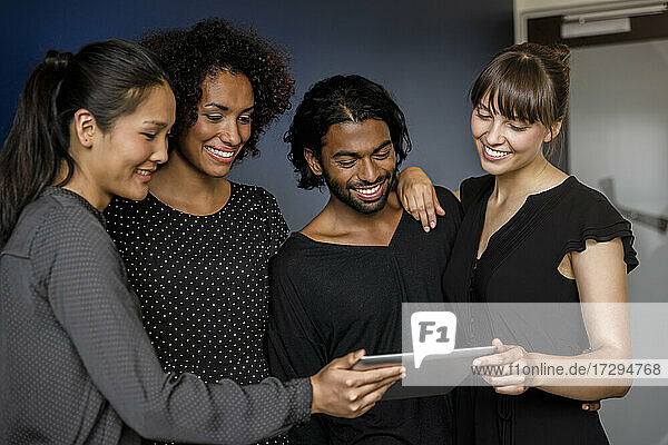 Lächelnder männlicher und weiblicher Unternehmer  die sich ein digitales Tablet teilen  während sie sich im Büro unterhalten