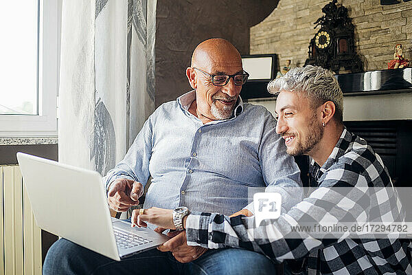 Smiling father and son sharing laptop while sitting together at home