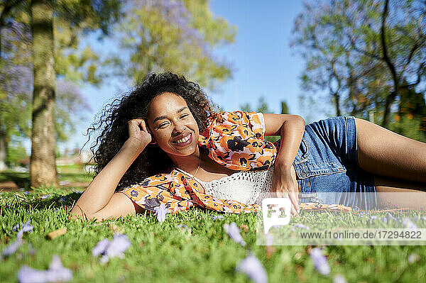 Smiling woman lying on side in park on sunny day