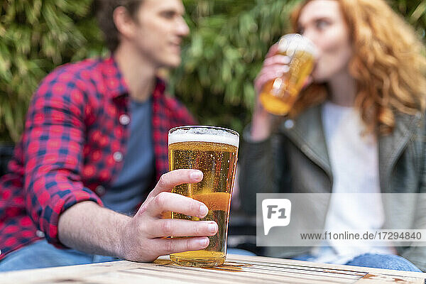Mann hält Bierglas  während er mit seiner Freundin in einer Kneipe sitzt