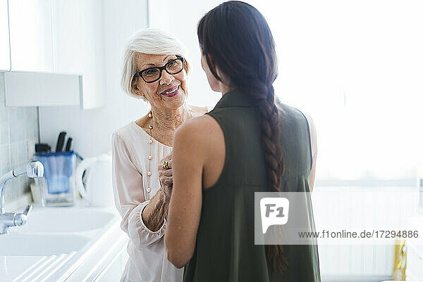 Lächelnde ältere Frau im Gespräch mit ihrer Enkelin in der Küche zu Hause