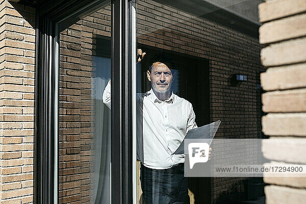Geschäftsmann mit Dokumenten durch Glasfenster eines Hauses gesehen