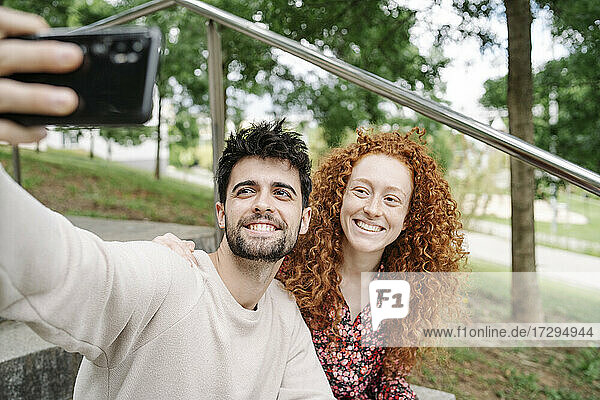 Lächelndes junges Paar  das ein Selfie mit seinem Mobiltelefon in einem öffentlichen Park macht