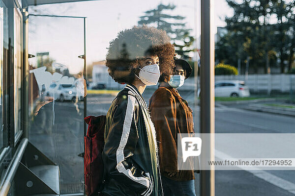 Freunde mit Gesichtsmaske warten am Busbahnhof bei Sonnenuntergang