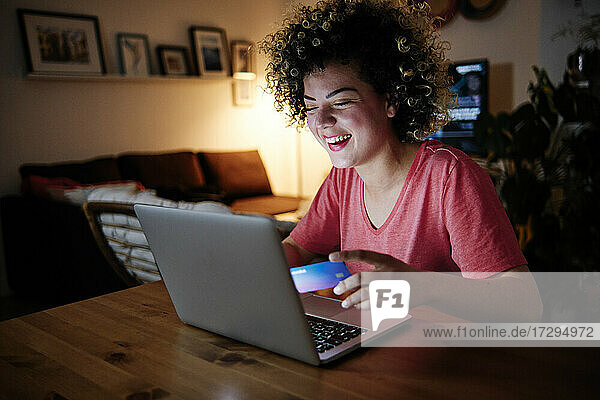 Fröhliche junge Frau mit Laptop beim Online-Shopping zu Hause