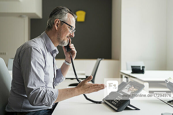 Männlicher Unternehmer im Gespräch mit einem Kollegen über ein VoIP-Telefon im Büro