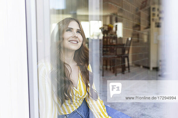 Lächelnde schöne Frau  die wegschaut  gesehen durch ein Fenster