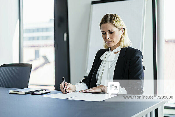 Blond businesswoman writing while sitting at desk in office