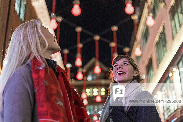 Lächelnde Freundinnen mit Blick auf die Weihnachtsbeleuchtung während der Feiertage