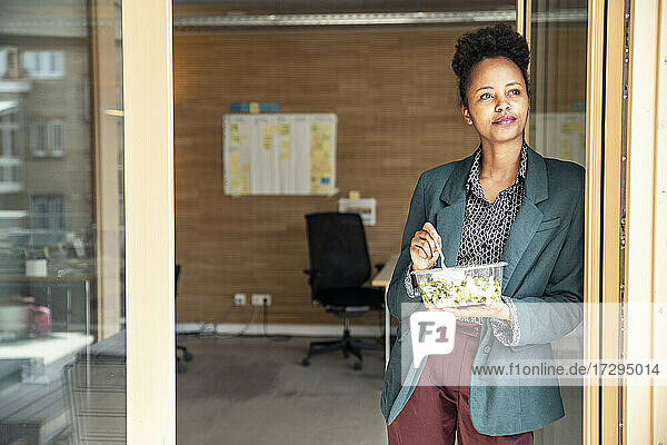 Geschäftsfrau mit Schüssel  die wegschaut  während sie sich im Büro an den Türrahmen lehnt